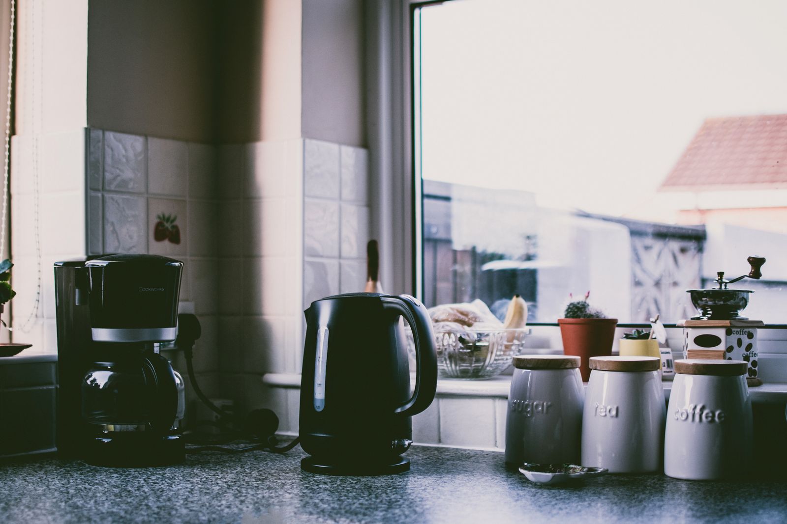 A kitchen bench by a window, with a kettle and tea and coffee canisters.
