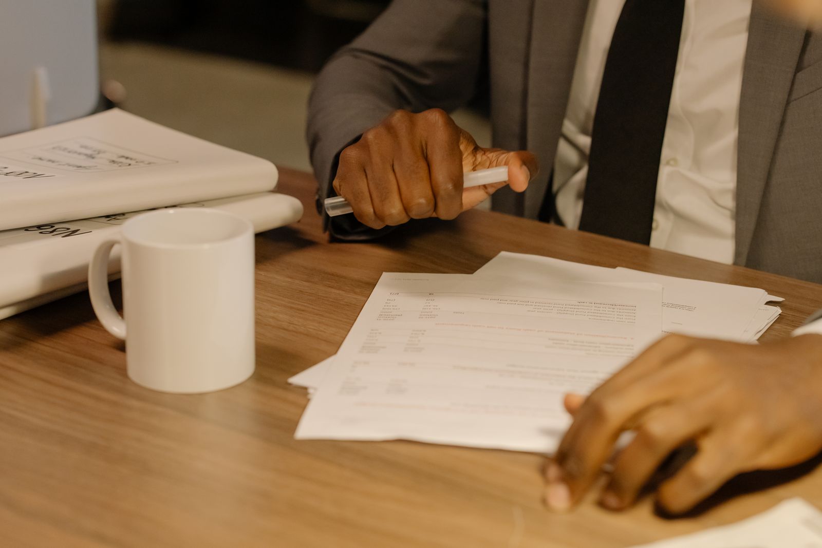 Hands passing a printed document across a desk beside a mug.