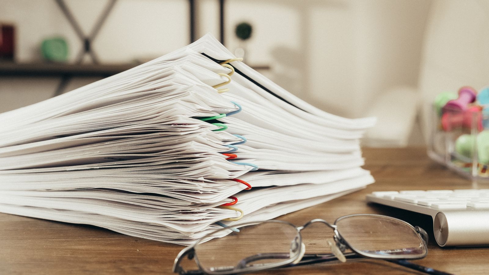 Stacks of paper-clipped documents on a desk beside a pair of reading glasses.