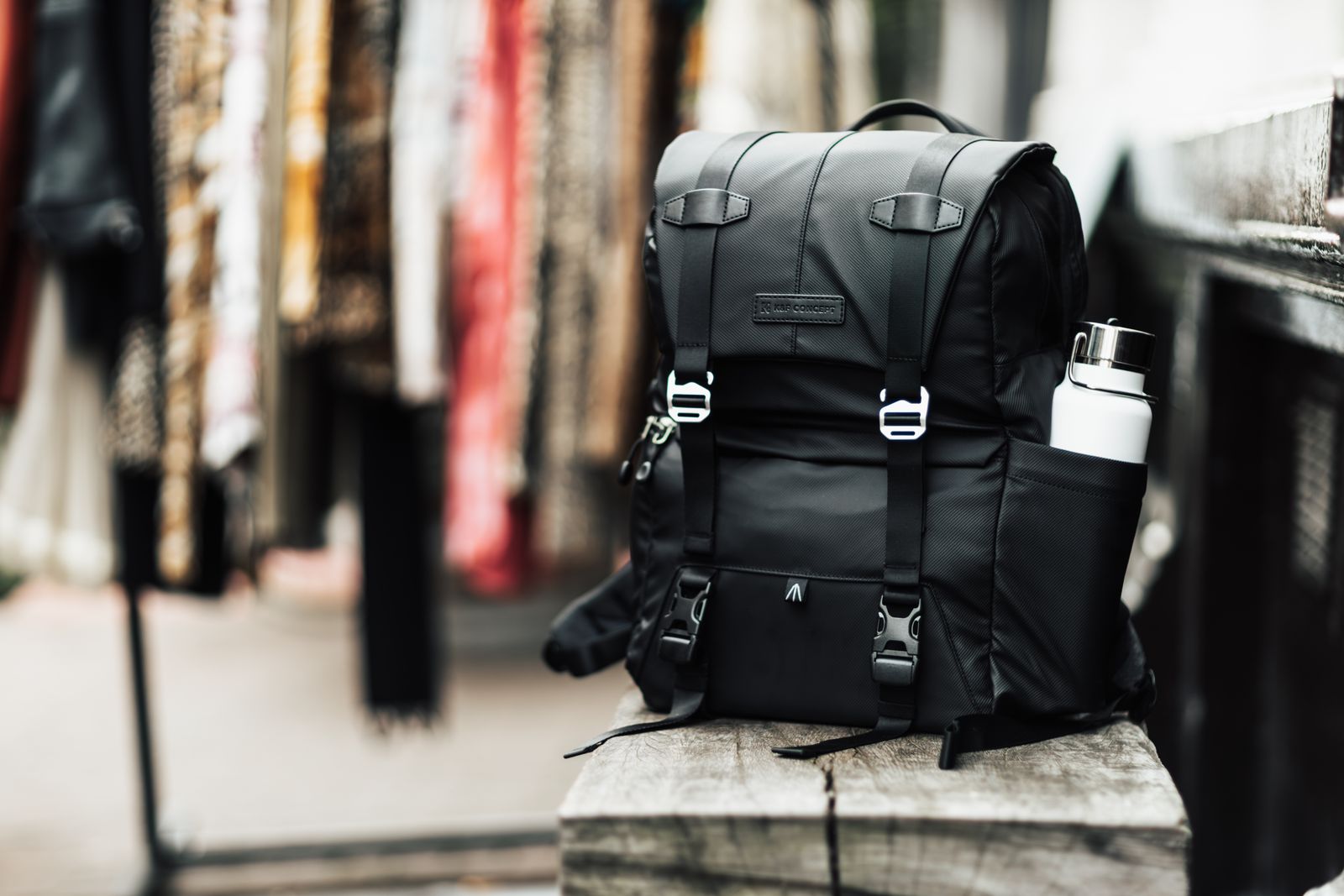 A backpack with a water bottle resting on a wooden bench outdoors.